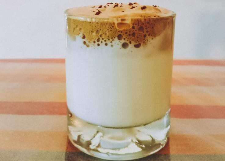 Frothy Dalgona coffee with whipped cream atop, served in a clear glass, embodying the viral trend of 2024
